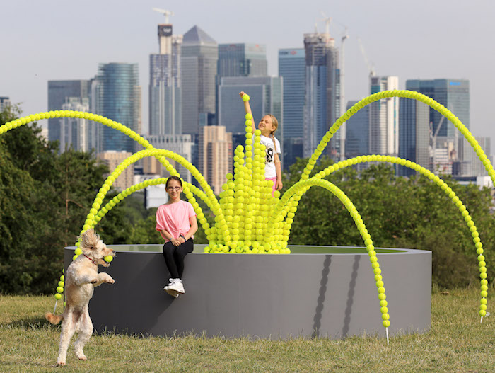 WaterAid and the Wimbledon Foundation have created a spectacular fountain of 2,631 tennis balls in Greenwich Park to mark the number of lives that could be saved on average each day if everyone everywhere had clean water and decent toilets. Lola Boorman, 7 from Lewisham pictured adding the finishing touches to the fountain this morning alongside Nelly Thurston, 9, also from Lewisham and  Monty the cockapoo. Two weeks before the start of The Championships, Wimbledon 2019, the remarkable tennis ball installation that overlooks the London skyline is a poignant reminder of the huge numbers of people around the world who could be enjoying a healthy future if only they had clean water close to home.    Across the world, 1 in 10 people don’t have clean water and 1 in 4 lack access to a decent toilet. Without these basic necessities children often miss school due to the burden of water collection or water-related illnesses and every day, thousands of lives are lost.     Each tennis ball that makes up the fountain represents a death that could be prevented if everyone everywhere had clean water, decent toilets and good hygiene.    The partnership between WaterAid and the Wimbledon Foundation is helping to make clean water, decent toilets and good hygiene normal for health centres, schools and communities in Ethiopia, Malawi and Nepal. The fountain is part of their #TeamWater campaign.    Helen Parker, Head of the Wimbledon Foundation said:    "It’s hard to imagine life without access to clean water, yet for 1 in 9 people around the world, this is a daily reality, holding whole communities back from fulfilling their potential.     “Clean water and good sanitation are vital ingredients for health, education and success. The Wimbledon Foundation is proud to team up with WaterAid to champion water for everyone everywhere and help prevent lives being lost needlessly.”    Marcus Missen, Director of Communications and Fundraising at WaterAid, said:     “The striking fountain of tennis balls highlights the scale of the global water and sanitation crisis and the urgent need to tackle it together. Each of the 2,631 tennis balls on the fountain represents one human life that could be saved on average every single day if everyone everywhere had access to clean water and decent toilets.      “By working together with the Wimbledon Foundation to provide clean water, we are helping transform lives and ensure healthier futures for generations to come.”      Ketilina Nyundo, 37, a mother of three from Malawi, said her life was transformed when WaterAid helped bring water to her village.     Ketilina said:    “Since we received a bore hole in the village, life has never felt better. As a community, we have had our livelihoods elevated. More children are going to school. People are now able to build better houses. As a mother, I am now proud to be able to support my children. Unlike in the past where they had to report late for their classes, things have improved now. On top of that, they are doing quite well in school.”    Local schoolchildren from South East London, Lola, 7, Nelly, 9, and Amelia May, 8, visited the fountain to support the #TeamWater campaign.   The fountain installation will also be on display at this year’s Championships which begin on 1 July. The tennis balls for this installation were gifted by Slazenger, the Official Ball of The Championships, and will be recycled following The Championships.    For further information: www.wateraid.org/uk/wimbledon